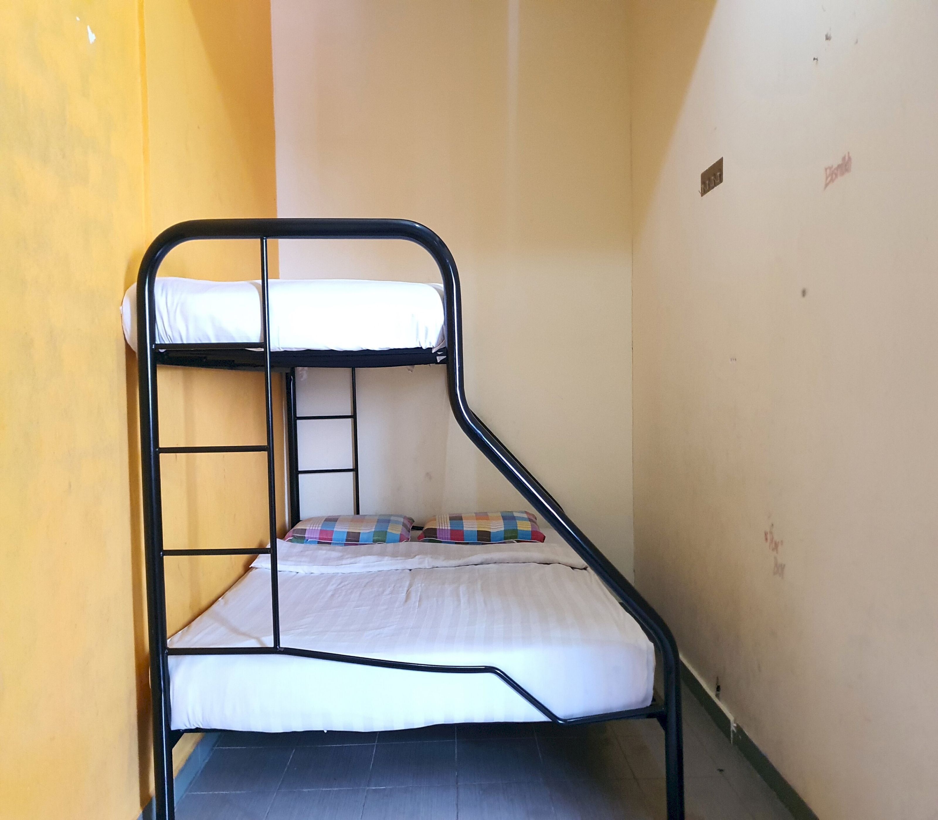 A bunk bed in a narrow room with yellow walls and a tiled floor.