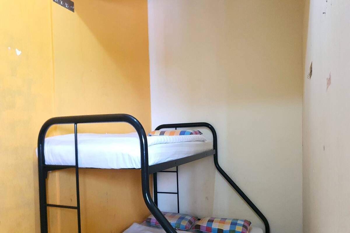 A bunk bed with a mattress and pillows, a metal ladder, and a yellow wall.