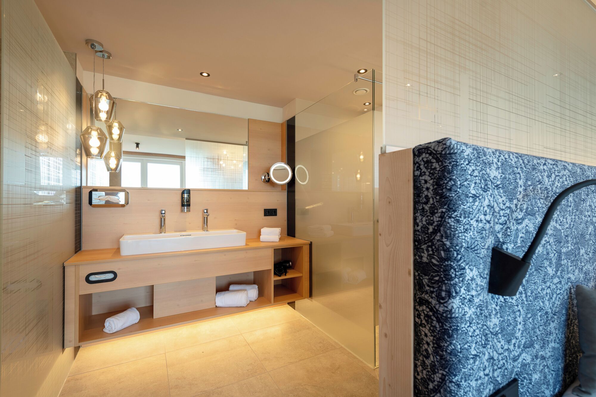 A modern bathroom with a large mirror, a white sink, wooden vanity, and a glass shower enclosure.
