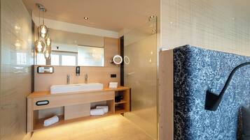 A modern bathroom with a large mirror, a white sink, wooden vanity, and a glass shower enclosure.