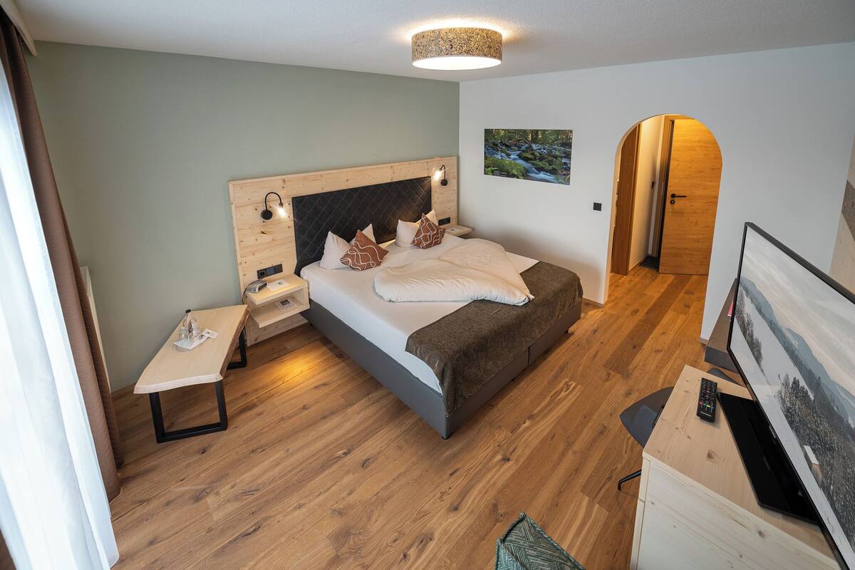 A modern bedroom with a bed, bedside tables, a desk, and a television.