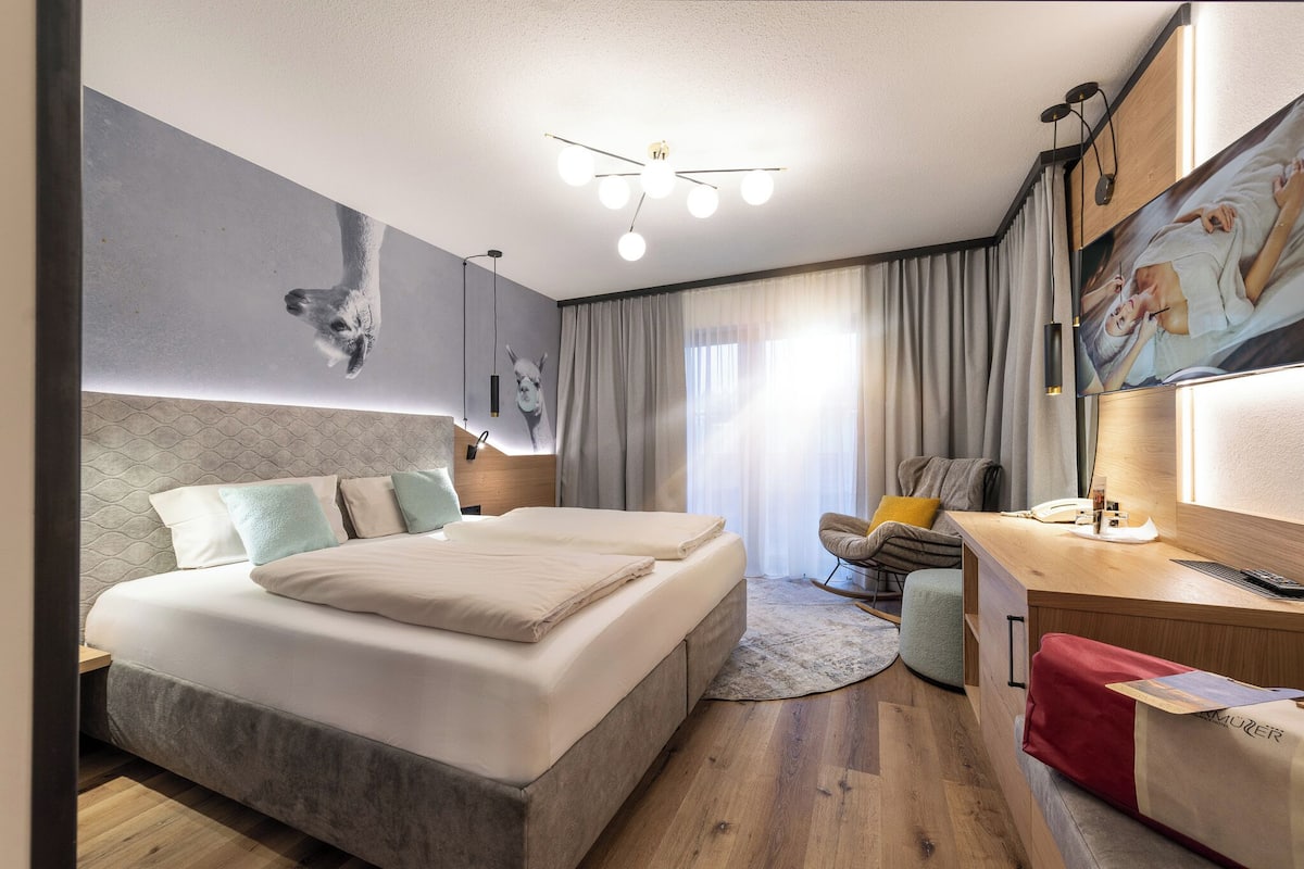A modern hotel room with a large bed, a desk, a chair, and artwork on the walls.