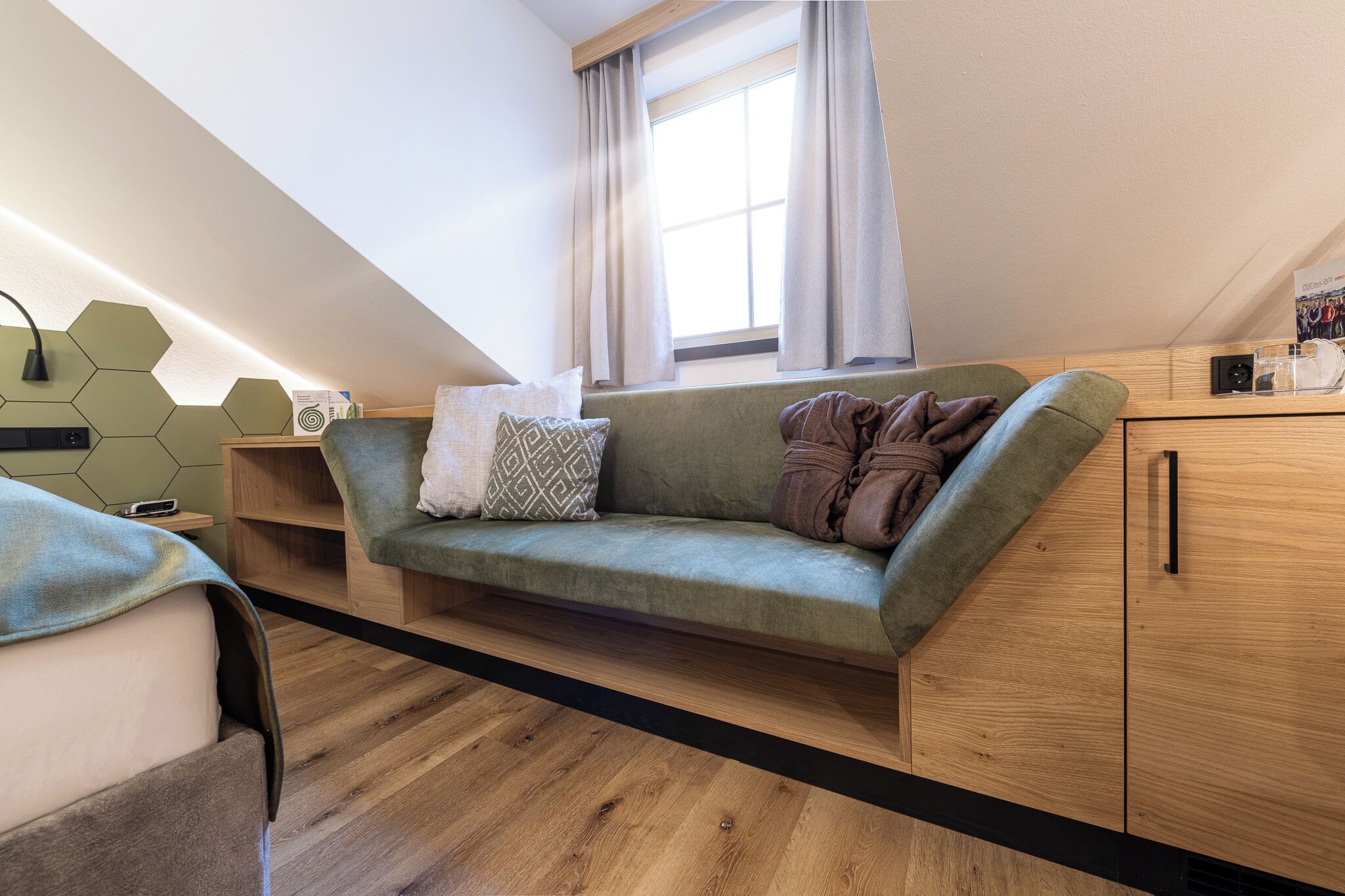 Una stanza moderna in stile loft con un divano verde, pavimento in legno e una finestra con tende.