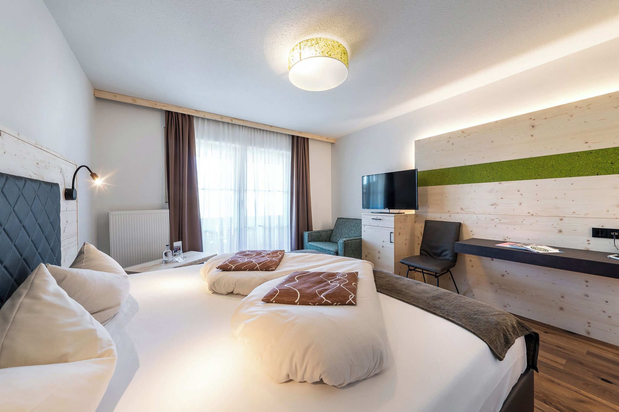 A modern hotel room with two beds, a desk, a television, and a window with curtains.