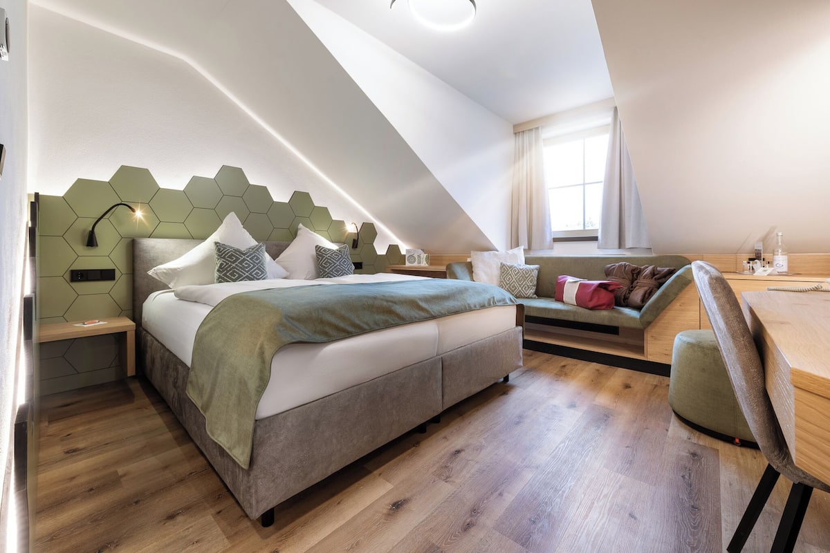 A modern bedroom with a bed, bedside tables, a desk, and a window.