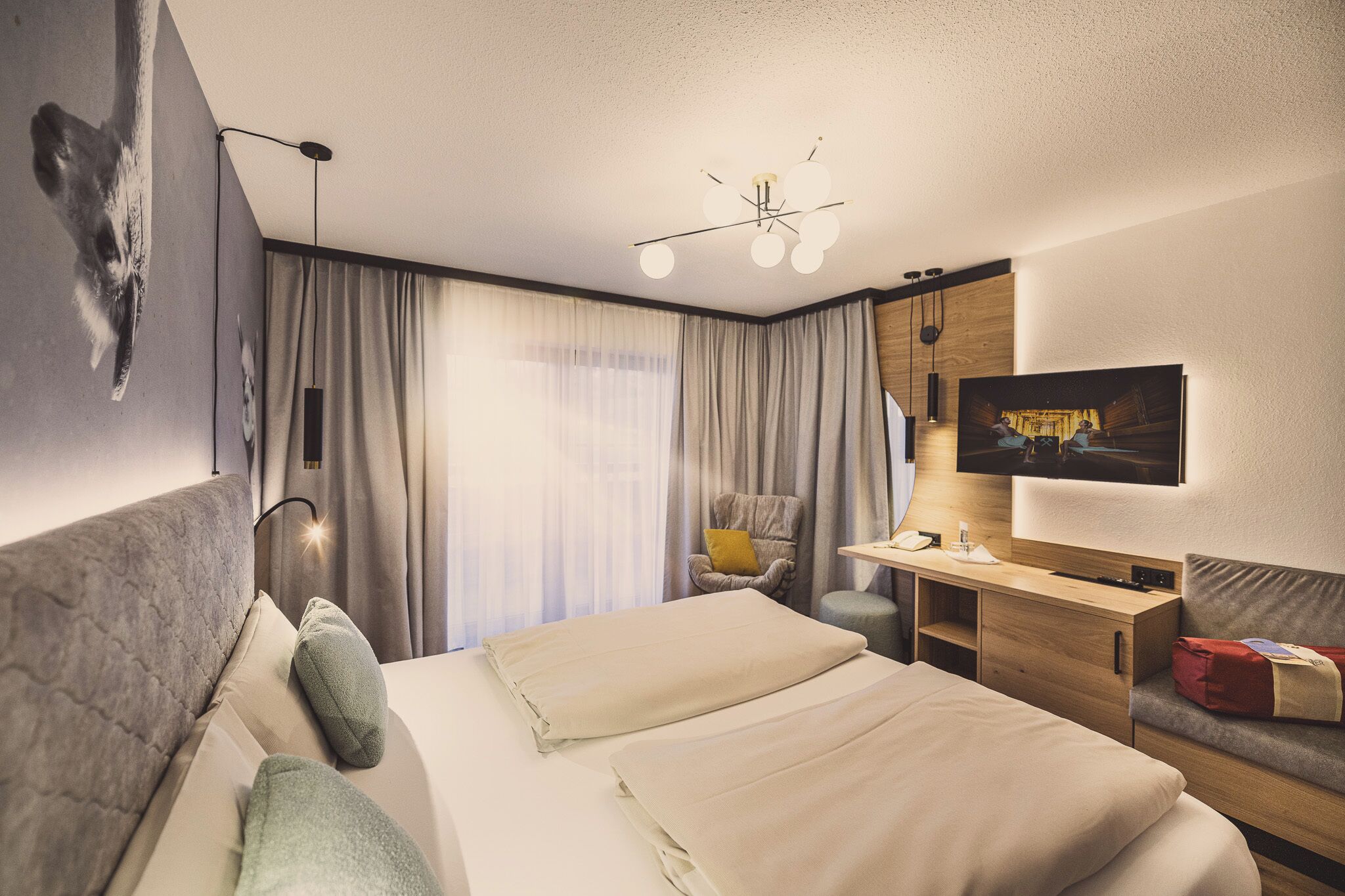Ein modernes Hotelzimmer mit einem großen Bett, einem Schreibtisch, einem Sessel, einem Fernseher und einer Deckenleuchte.