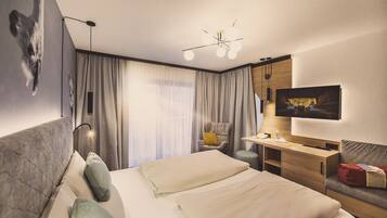 Ein modernes Hotelzimmer mit einem großen Bett, einem Schreibtisch, einem Sessel, einem Fernseher und einer Deckenleuchte.