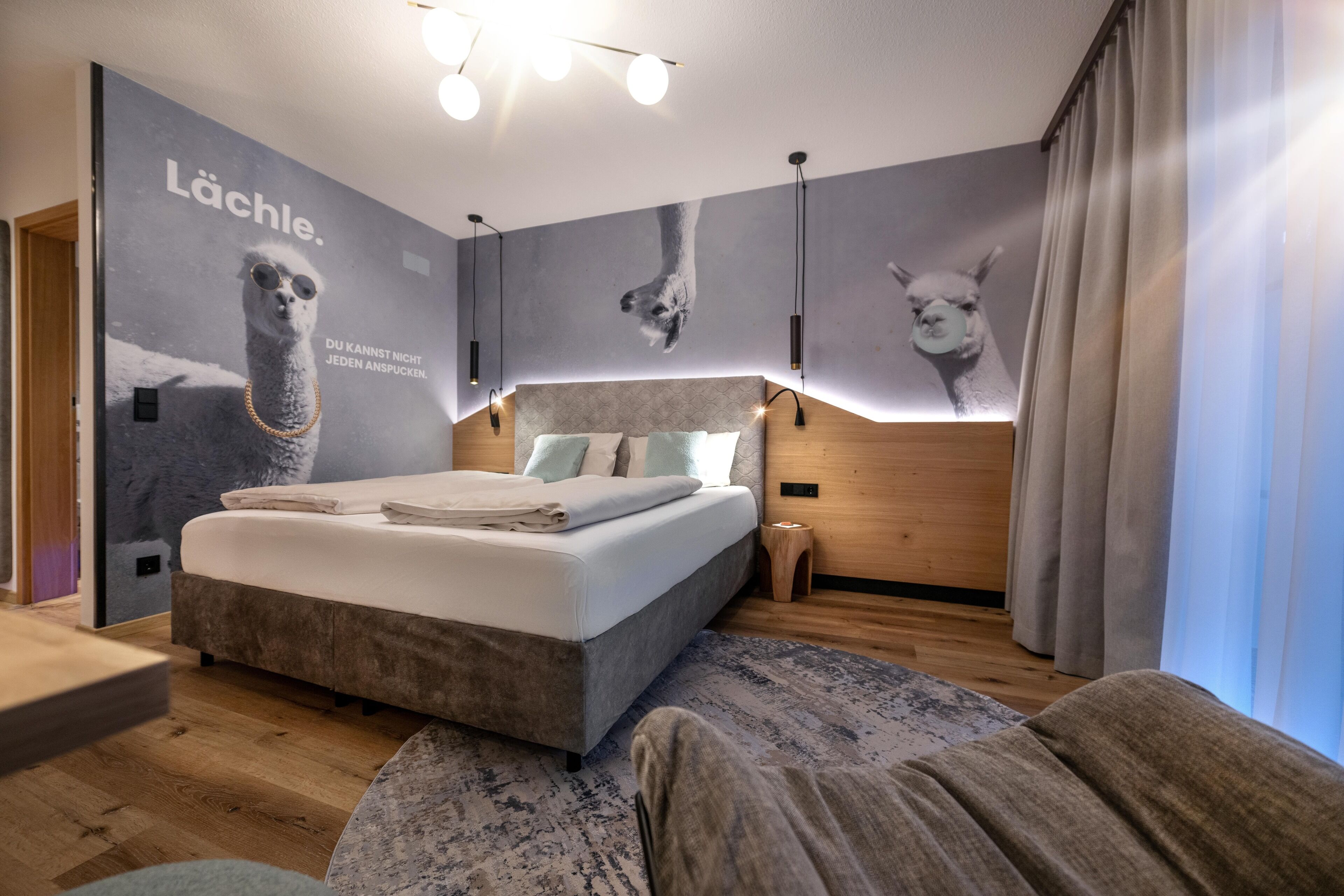 Un dormitorio moderno con una cama grande, un cabecero con iluminación integrada, una obra de arte en la pared de un llama y suelo de madera.