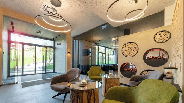 Un interior moderno con una mesa de centro de vidrio, sillas tapizadas en tonos verde y gris, y un elemento decorativo de madera.
