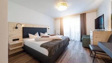 A modern hotel room with a large bed, a desk, a television, and a wooden headboard.