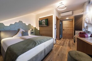 A modern hotel room with a large bed, a wooden headboard, a mounted TV, and a wooden door leading to a bathroom. - Landrefugium Obermüller (Untergriesbach)