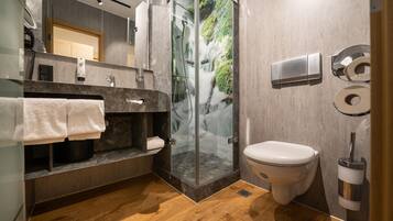 A modern bathroom with a glass-enclosed shower, a marble sink, a toilet, and a towel rack.