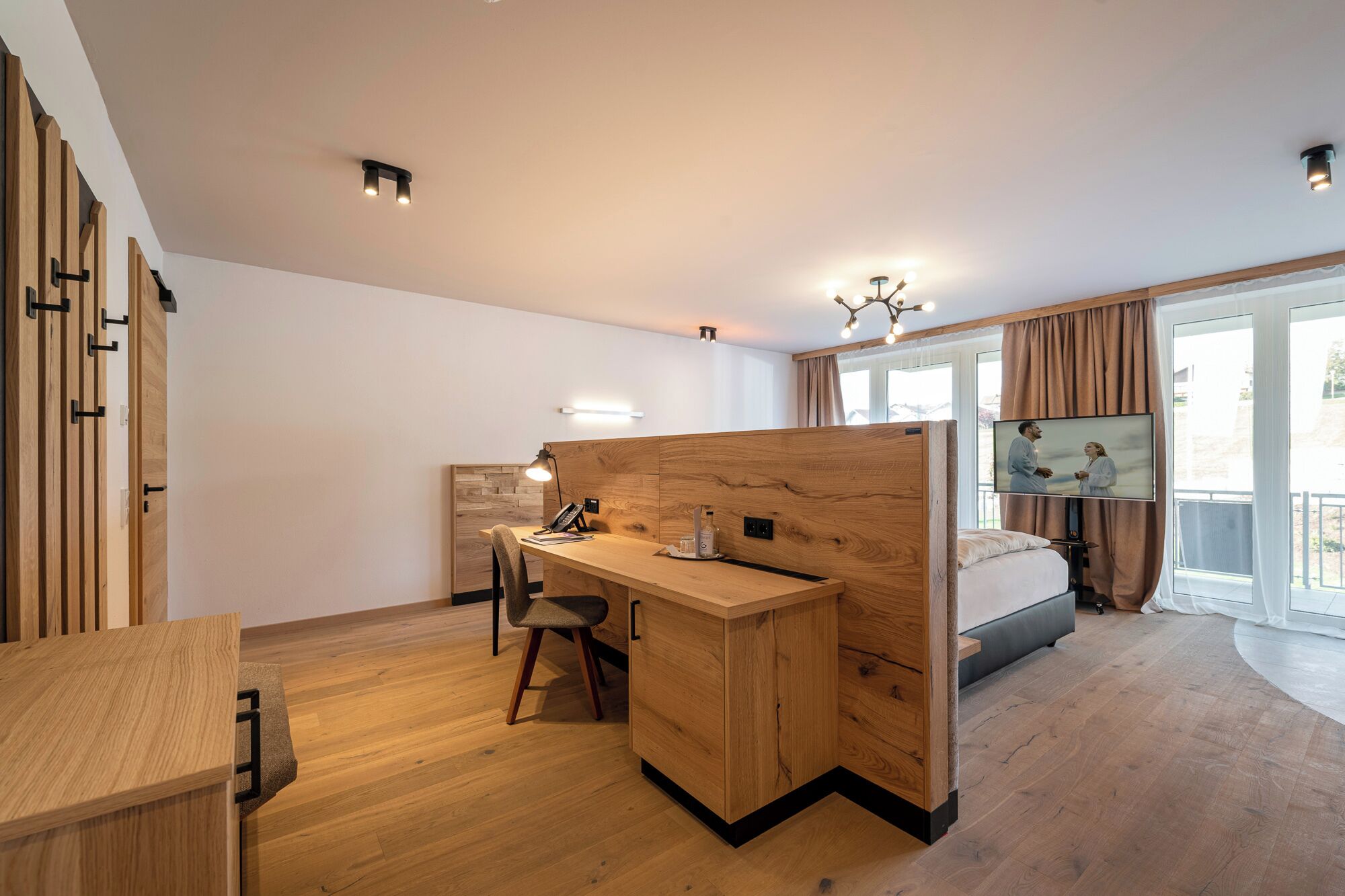 A modern bedroom with a wooden desk, a bed, and a TV.