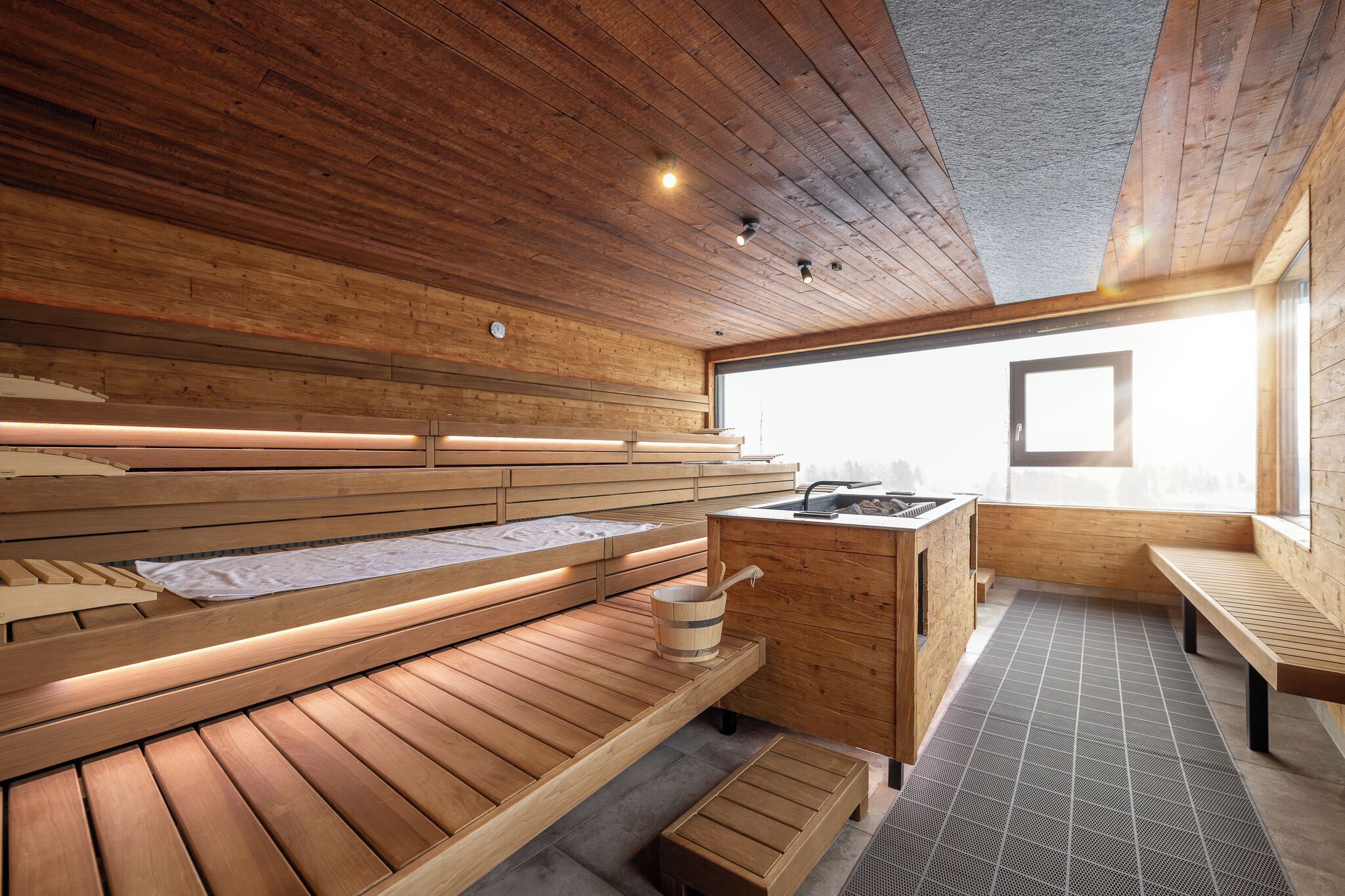 A sauna with wooden benches, a wooden cabinet, and a window providing natural light.
