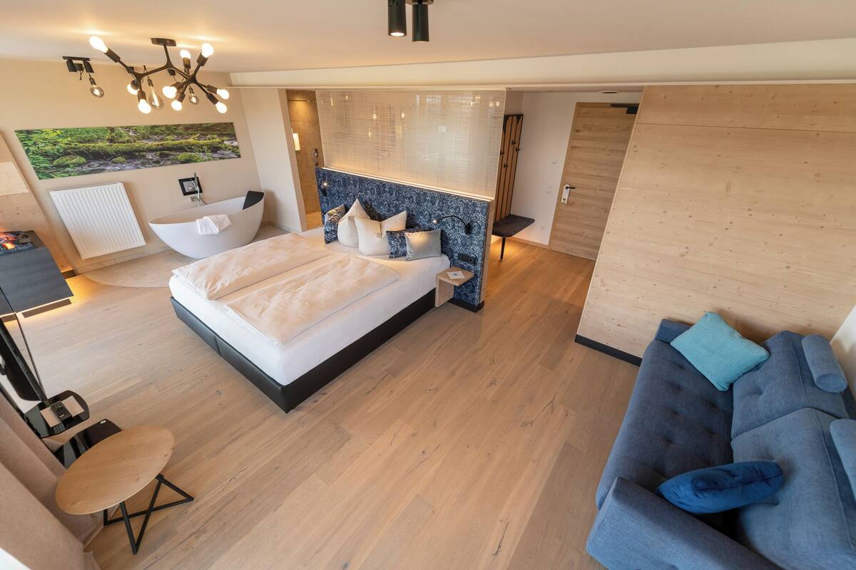 A modern bedroom with a large bed, a sitting area with a sofa, a small table, and a bathtub.