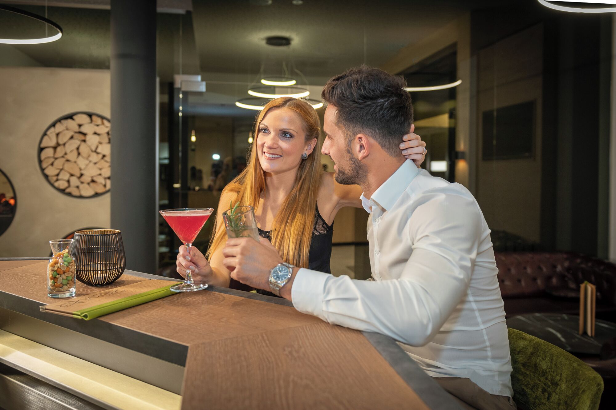 Una pareja sentada en una barra, con una copa de martini y una jarra de agua.