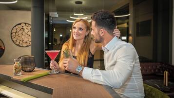 Una pareja sentada en una barra, con una copa de martini y una jarra de agua.