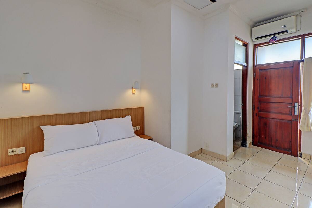 A neatly made bed with a wooden headboard, a bedside table, and two wall-mounted lights.