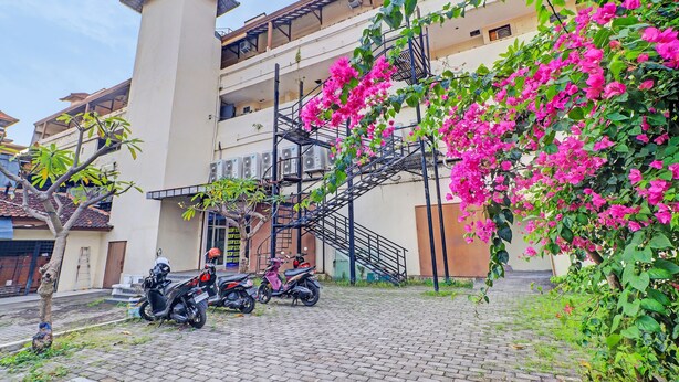 A building with a staircase and a tree with pink flowers. - Hotel O Simalem Guest House (Kuta)