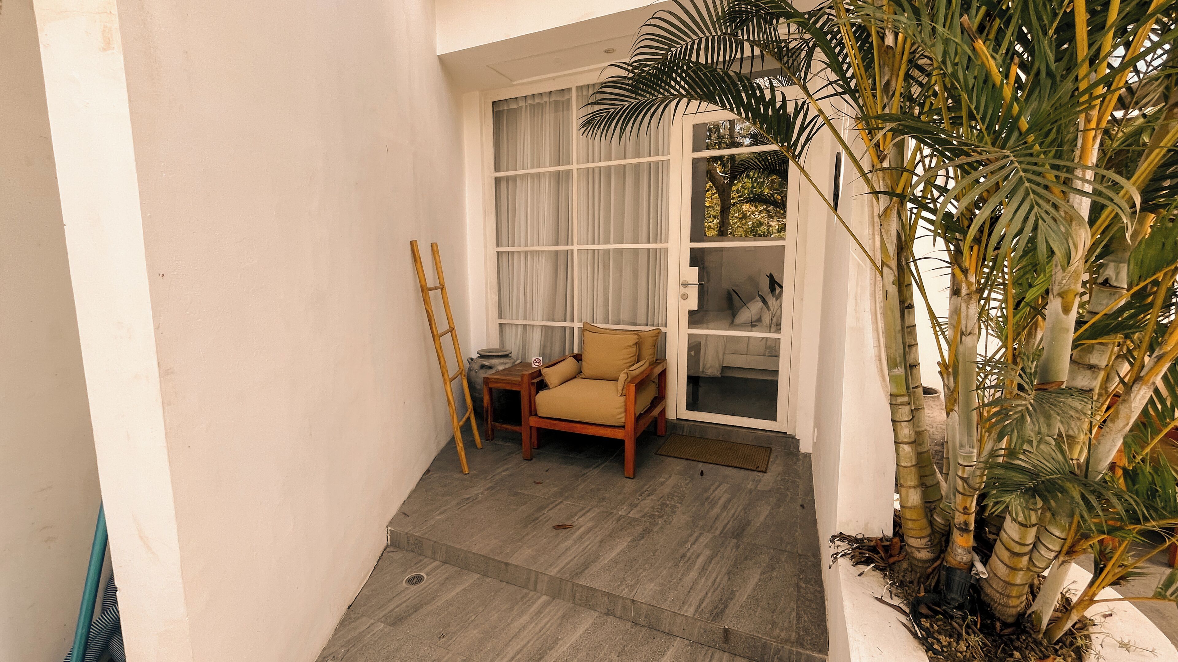 Un pequeño espacio al aire libre cercado, con una silla de madera, una escalera y una planta en maceta.
