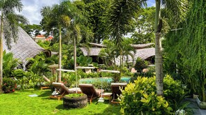 Un exuberante jardín con piscina, sillas de descanso y estructuras de techo de paja.