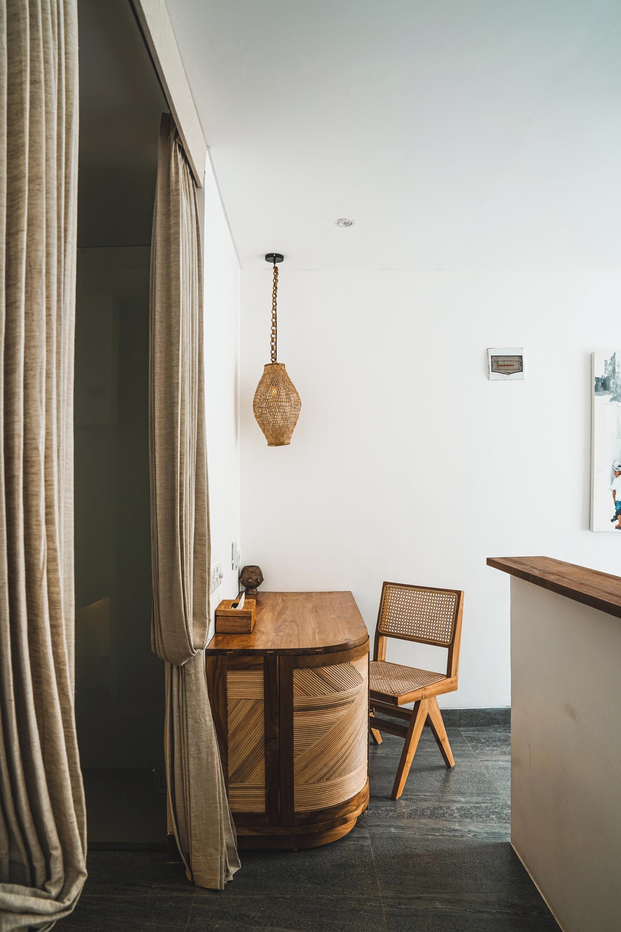 Una stanza con un tavolo rotondo in legno, una sedia in vimini, un lampadario e una porta socchiusa con tende.