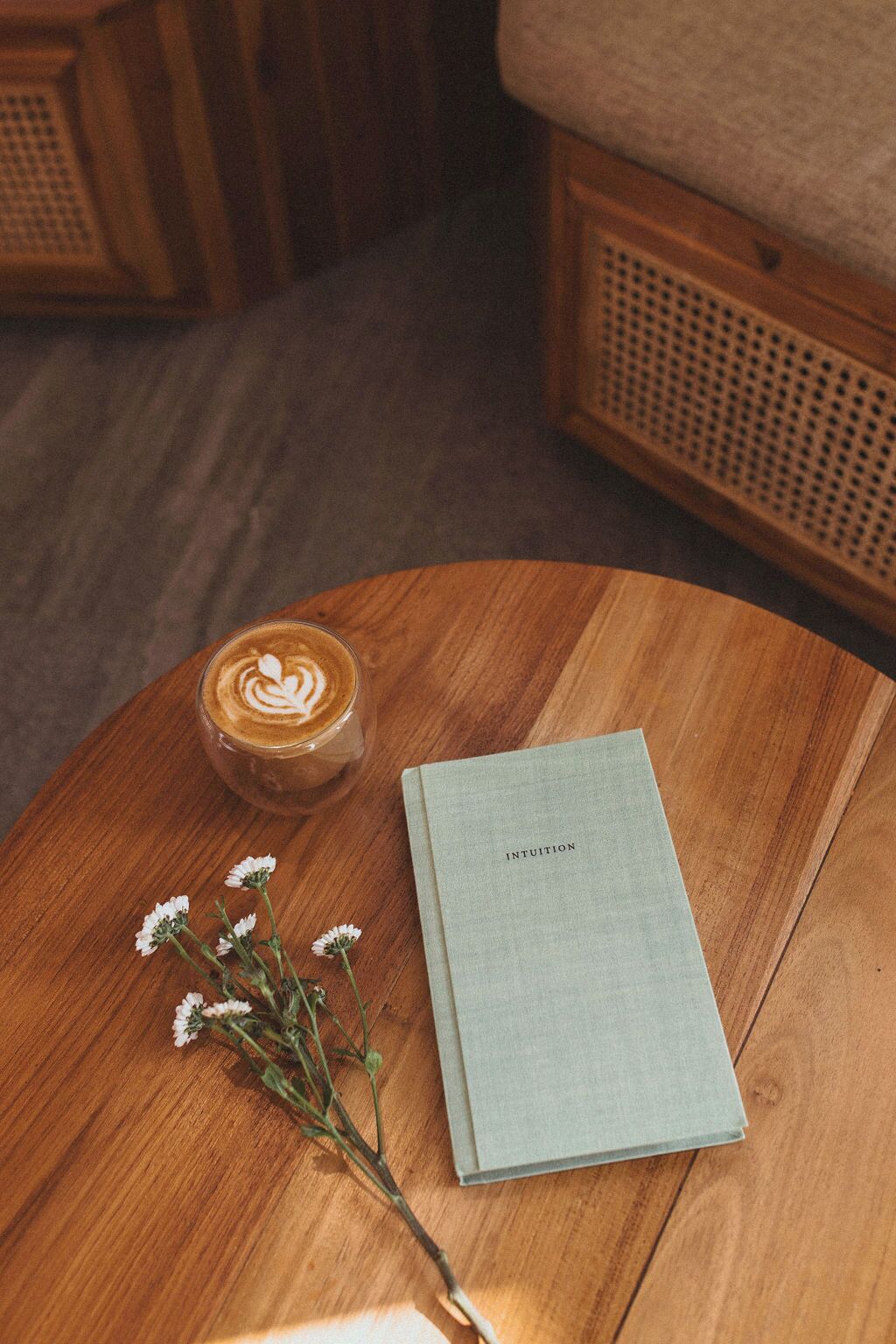 Un tavolo di legno con un latte macchiato, un quaderno con la scritta 'INTUITION' e un piccolo bouquet di fiori.
