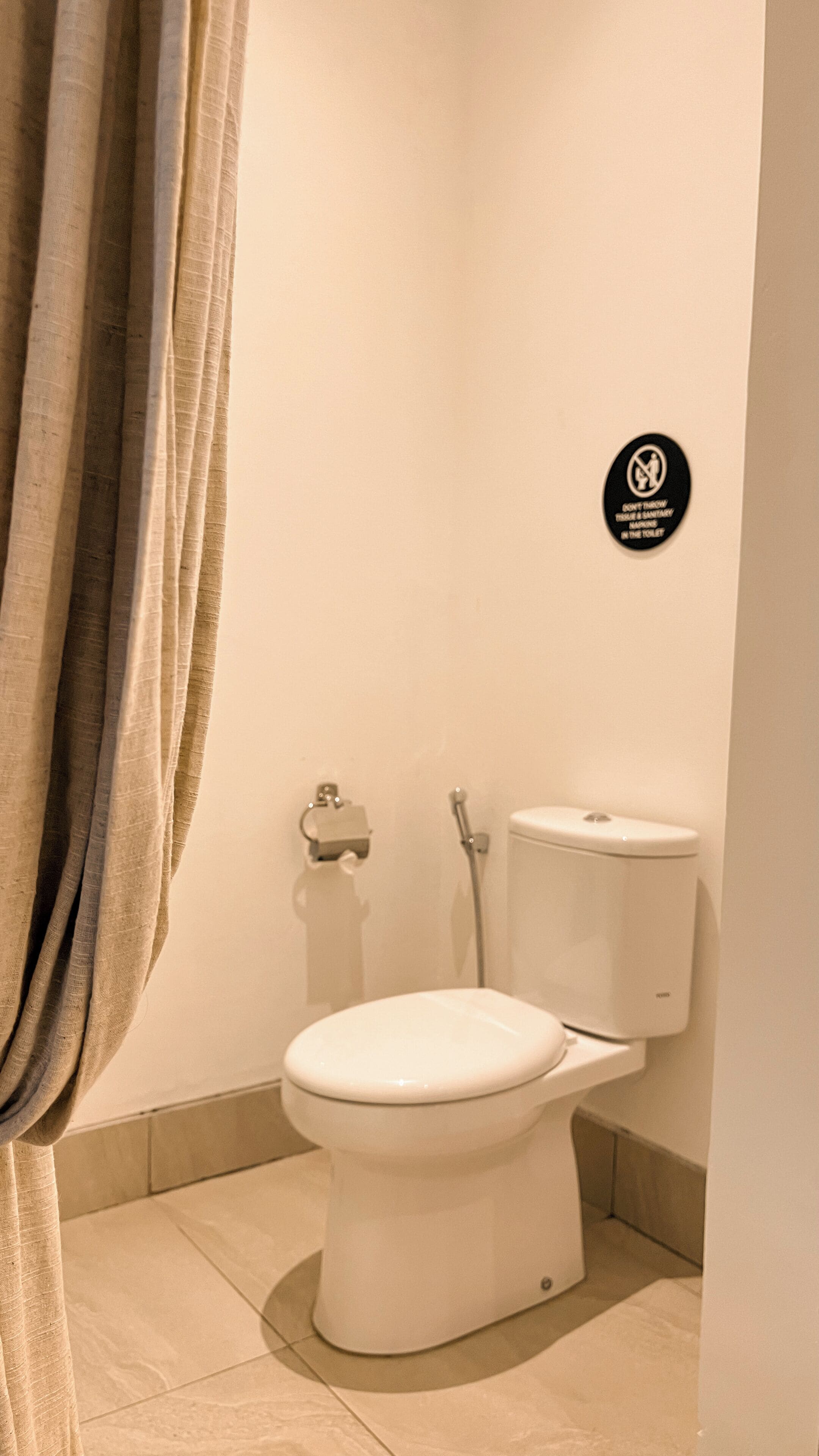 A bathroom with a toilet, a hand dryer, and a sign prohibiting the disposal of sanitary napkins in the toilet.
