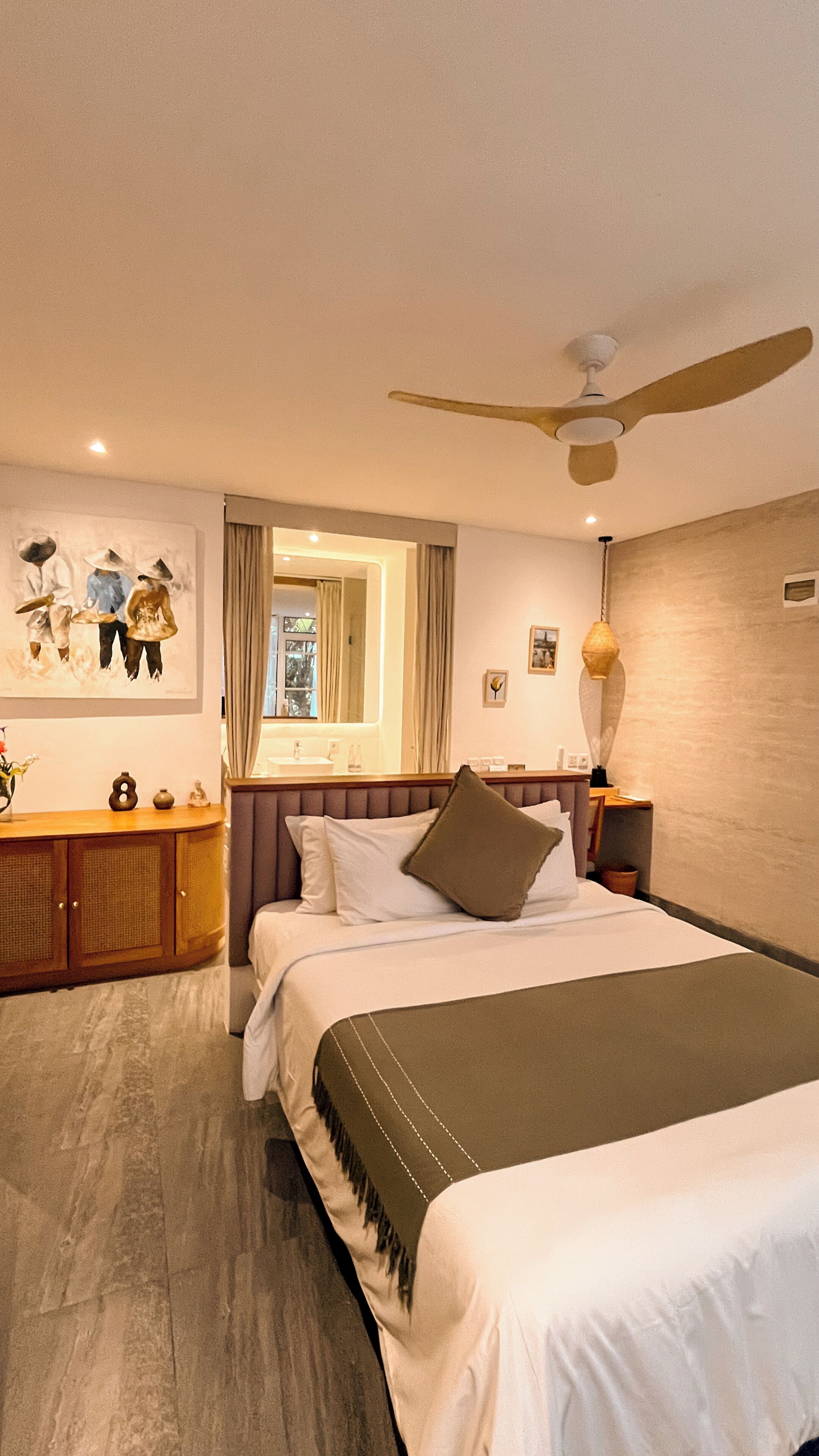 A hotel room with a bed, a ceiling fan, a large mirror, and artwork on the wall.