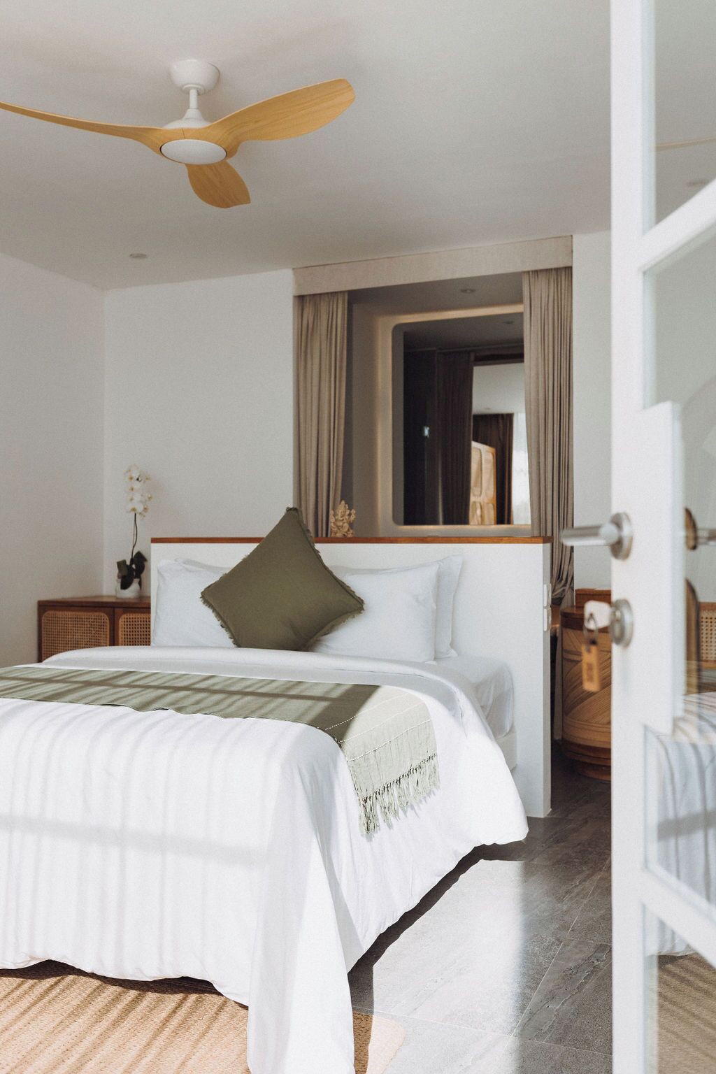 Un dormitorio con cama, ventilador de techo, ventana con cortinas y una puerta.