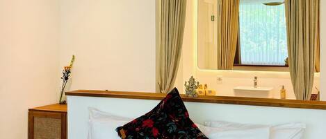 A hotel room with a bed, a green throw blanket, a floral pillow, a wooden nightstand, a mirror, and a ceiling fan.