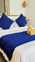 A neatly made bed with a blue striped blanket, two blue pillows, and a pair of yellow towels.