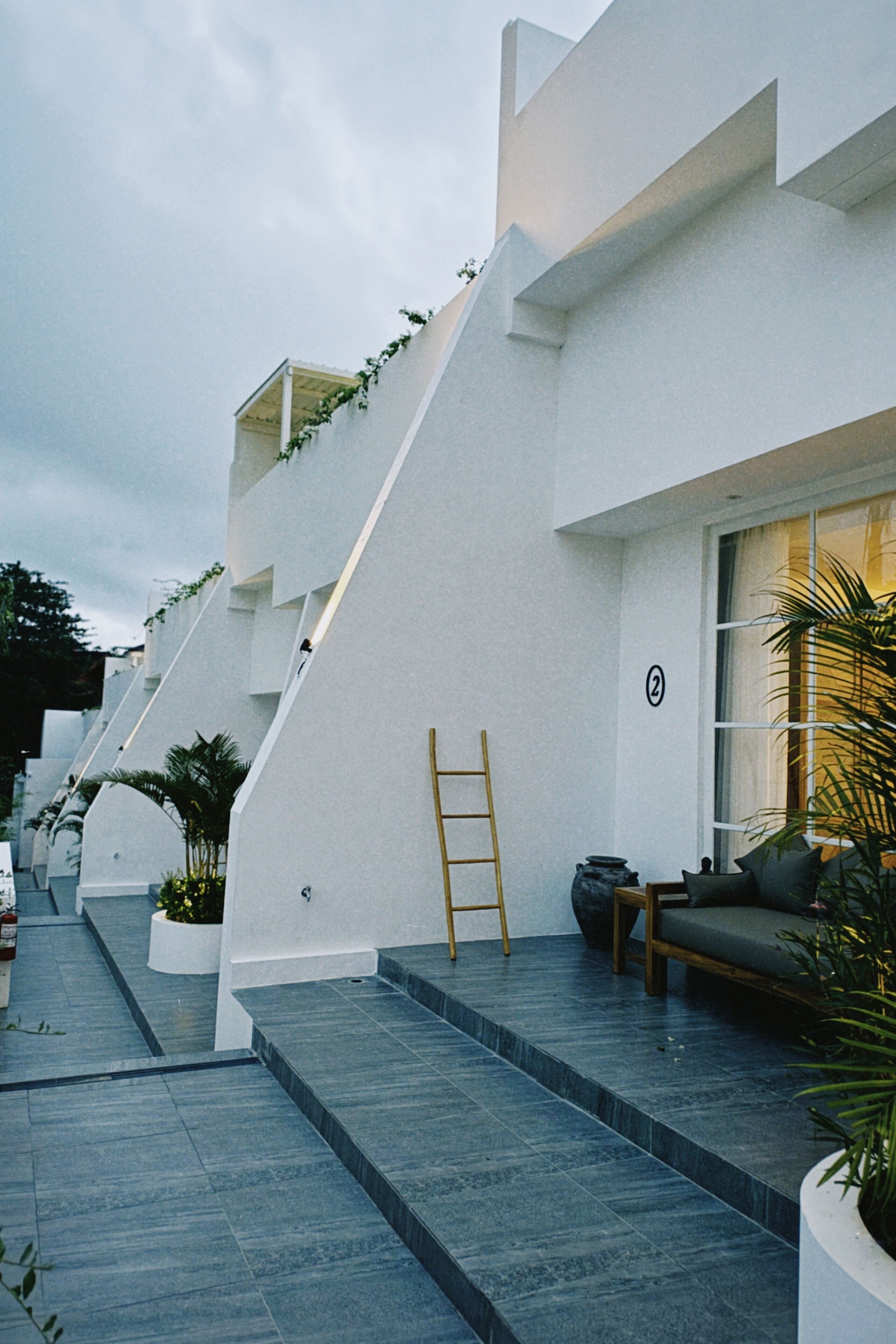 A modern building with a white exterior, a staircase leading to the entrance, and a bench outside.