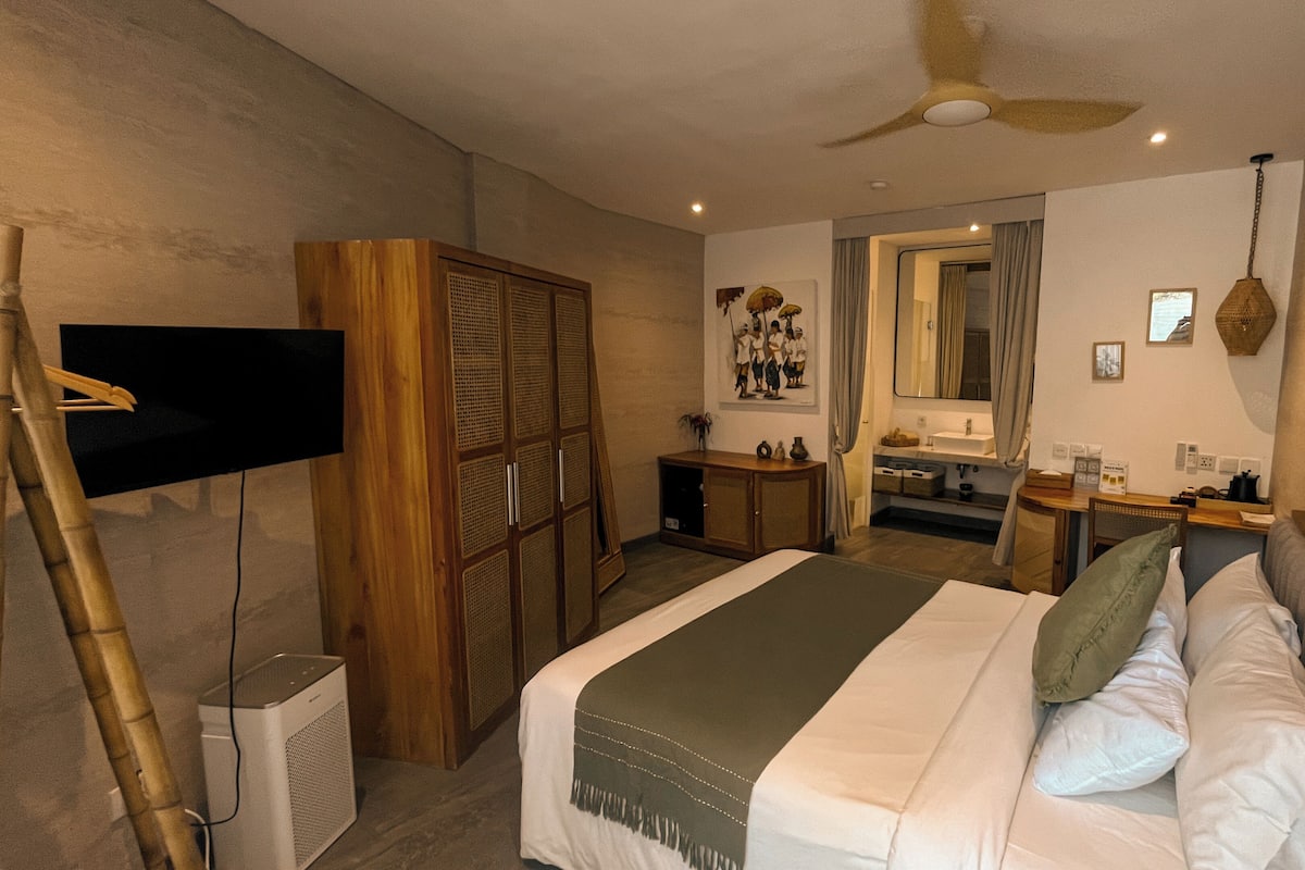 A bedroom with a bed, a desk, a mirror, a wardrobe, and a television.