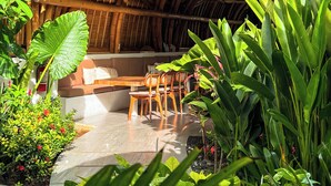 A bamboo structure with a curved roof, a dining area with wooden furniture, and lush tropical plants. - Mantra Wellness Centre (Pecatu)