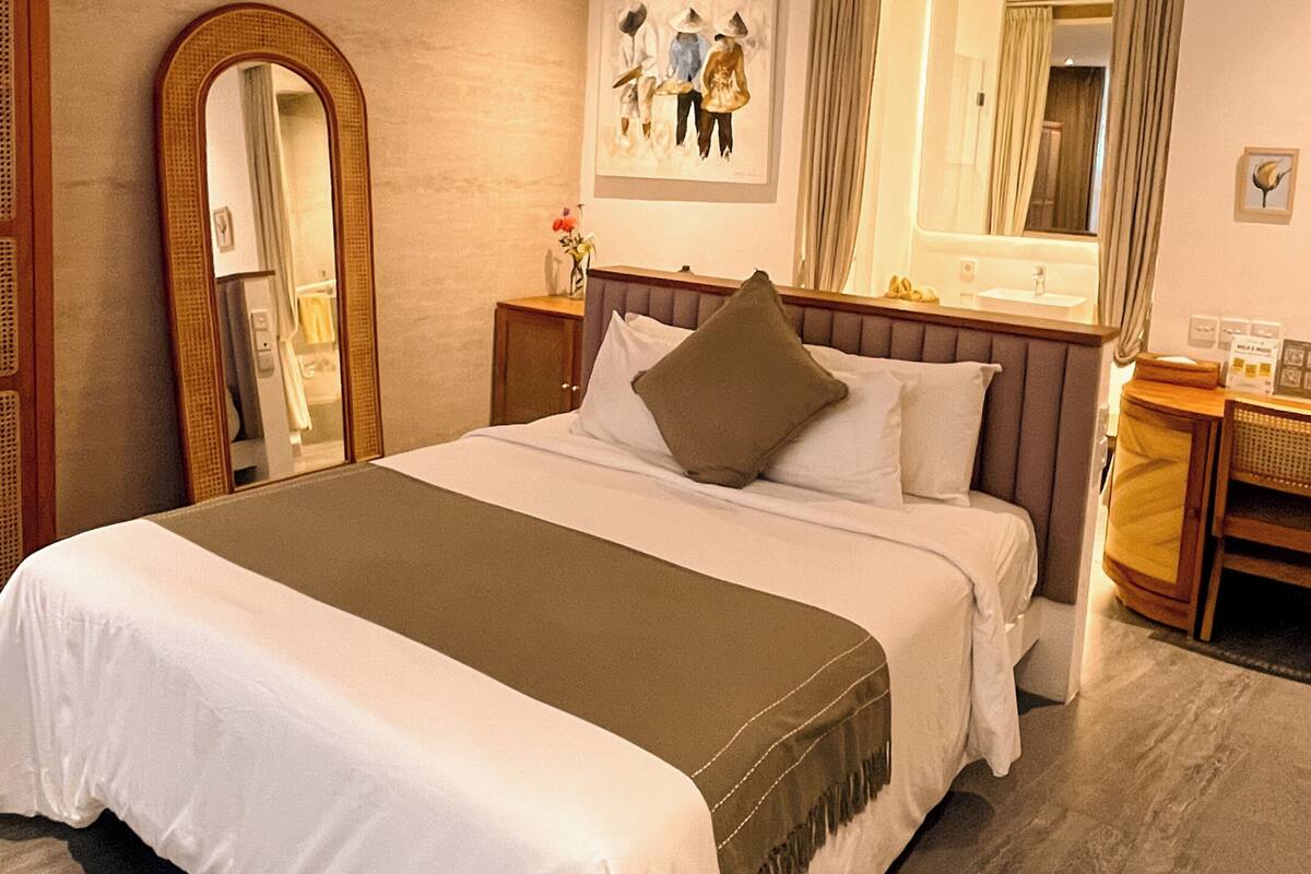 A hotel room with a bed, a ceiling fan, a large mirror, a desk, and a chair.