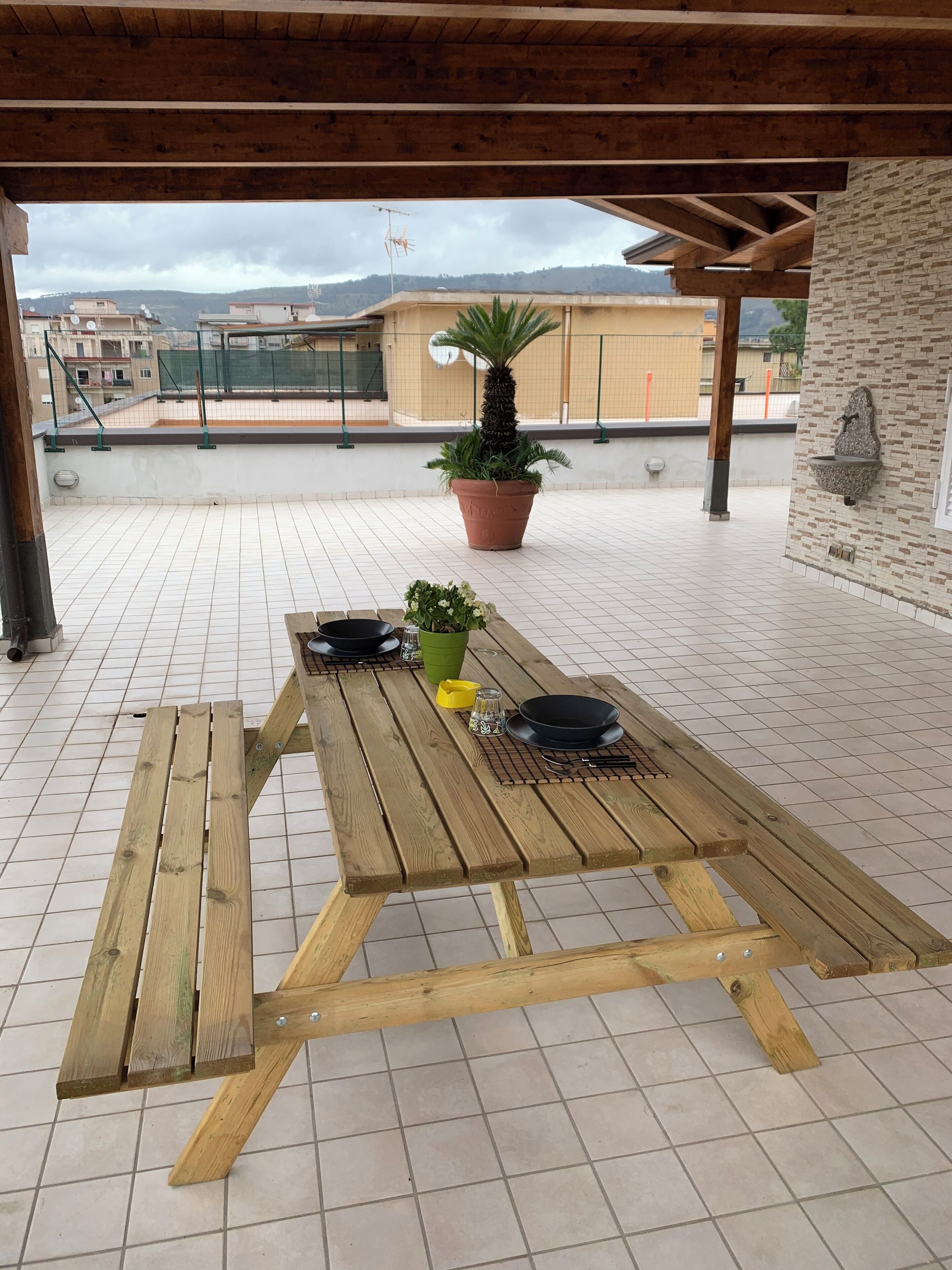A wooden table with a potted plant and a bowl on a tiled patio.