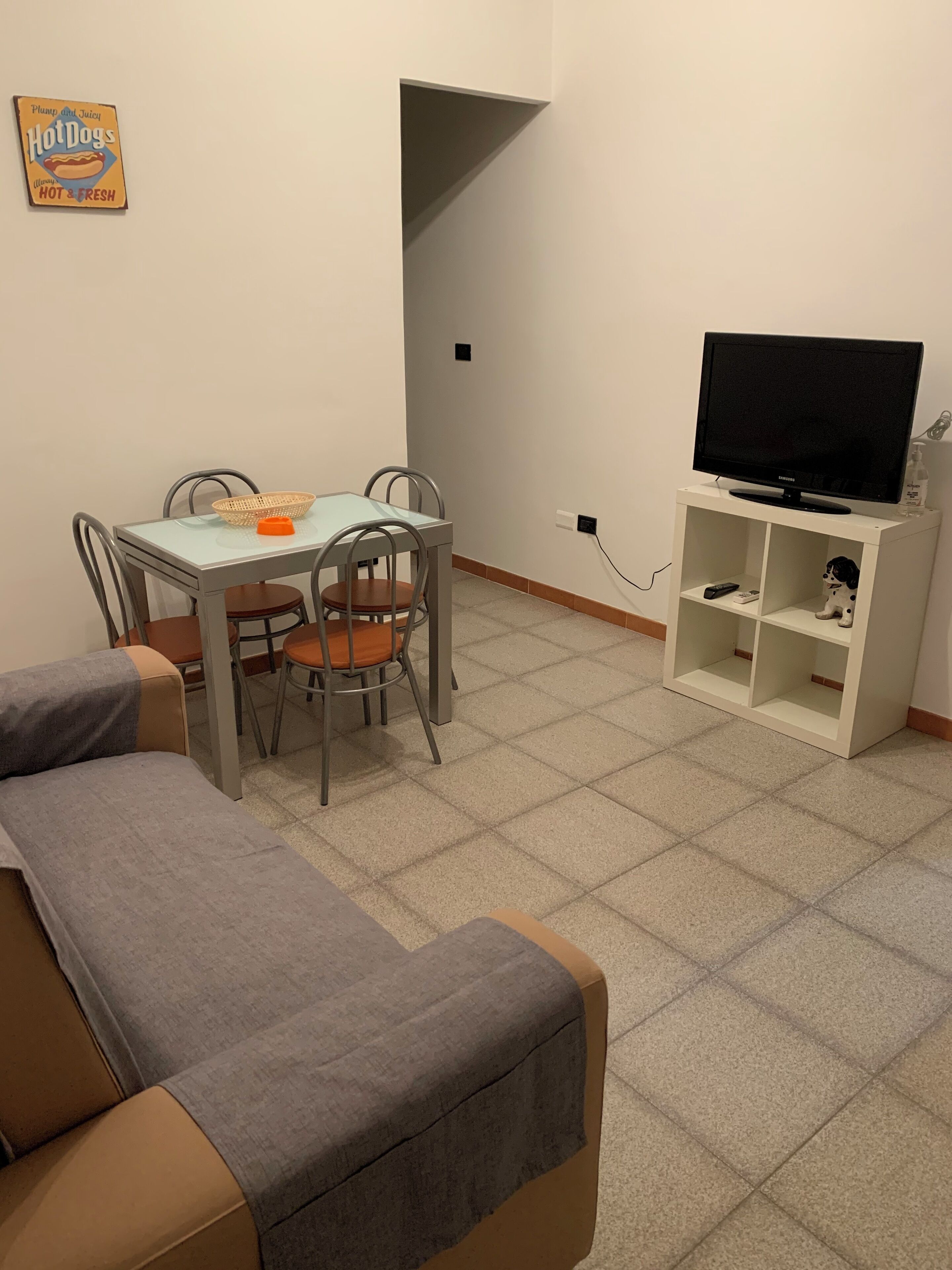 Un salon comprenant un canapé, une table à manger avec des chaises, un téléviseur posé sur un meuble et une petite étagère sur laquelle se trouve une figurine.