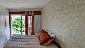 A hotel room with two beds, a balcony, and a view of greenery. - Maison Bonhage (Chaumont)