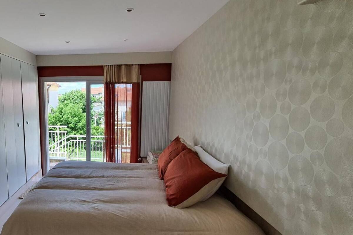 A hotel room with two beds, a balcony, and a view of greenery.