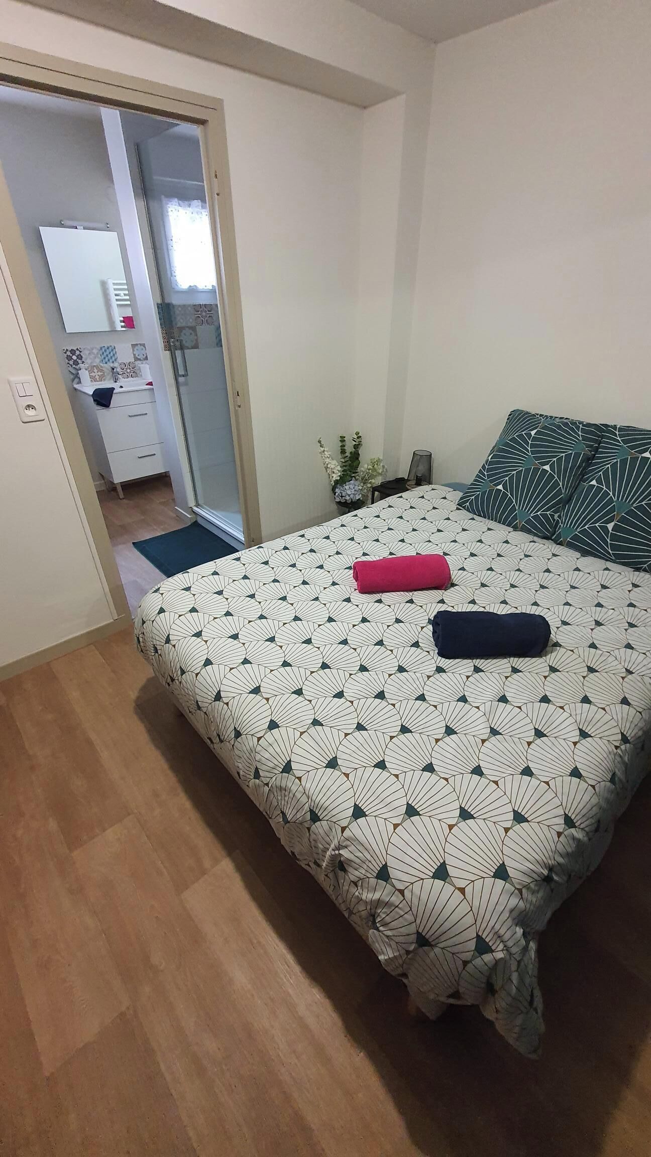 A bedroom with a bed, a nightstand, a mirror, and a bathroom visible through an open door.