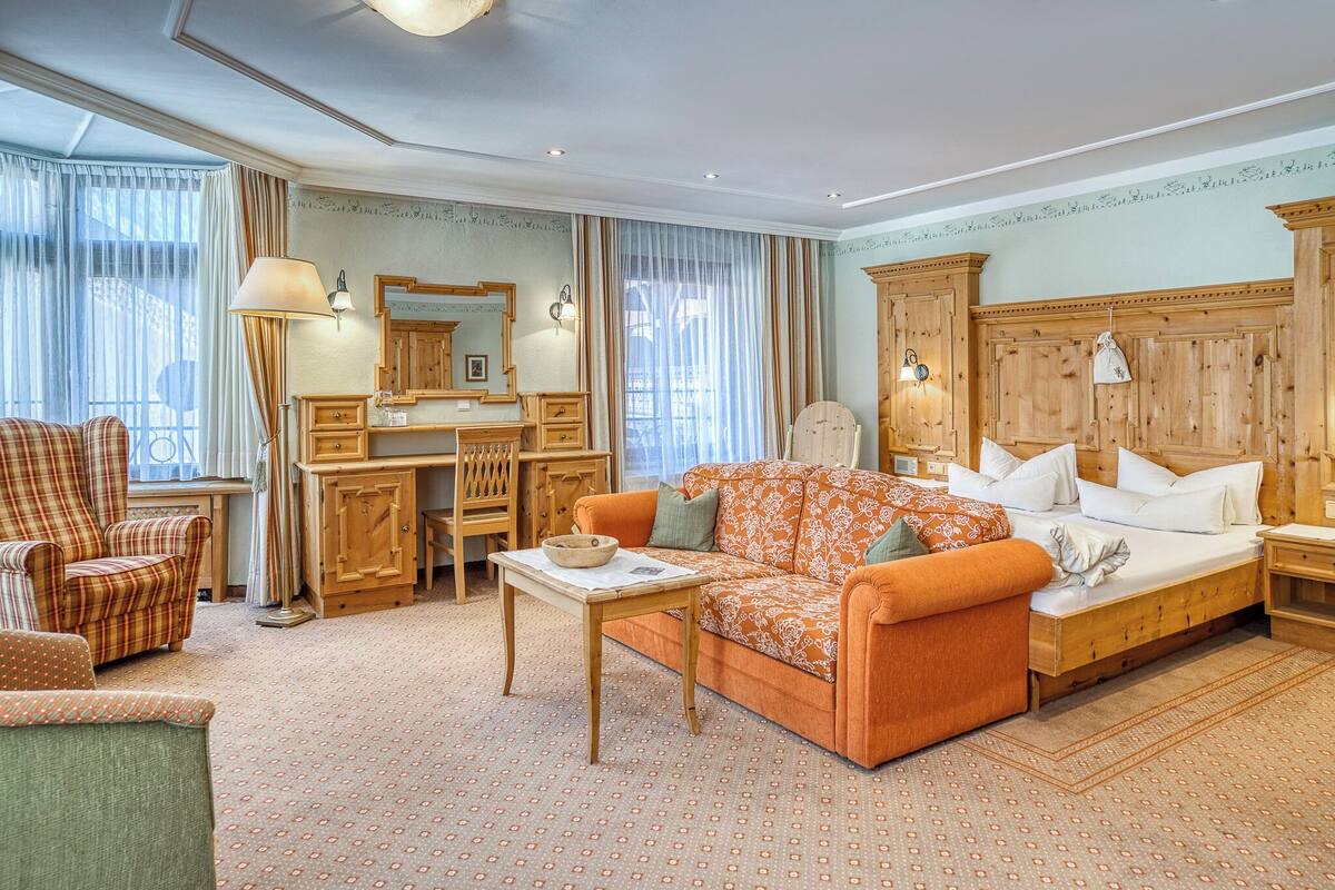 A room with a sofa, armchair, desk, and a large mirror.