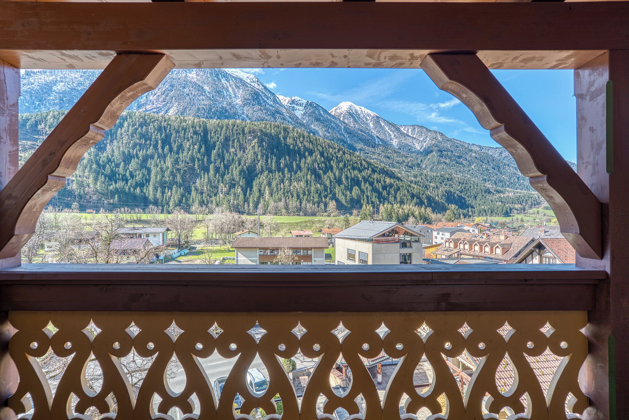 A mountain view through a wooden balcony with a decorative railing.