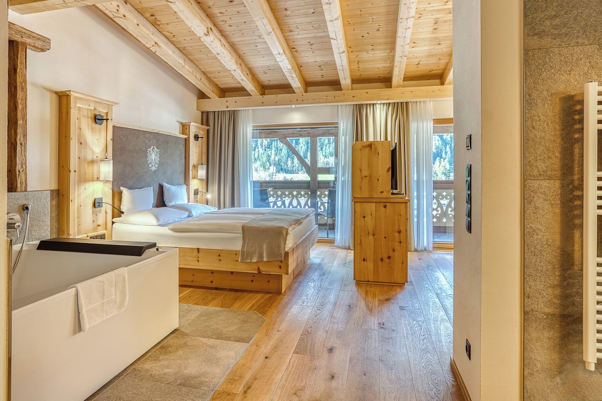 Interior de una cabaña de madera con una cama, un armario de madera y vistas al exterior.