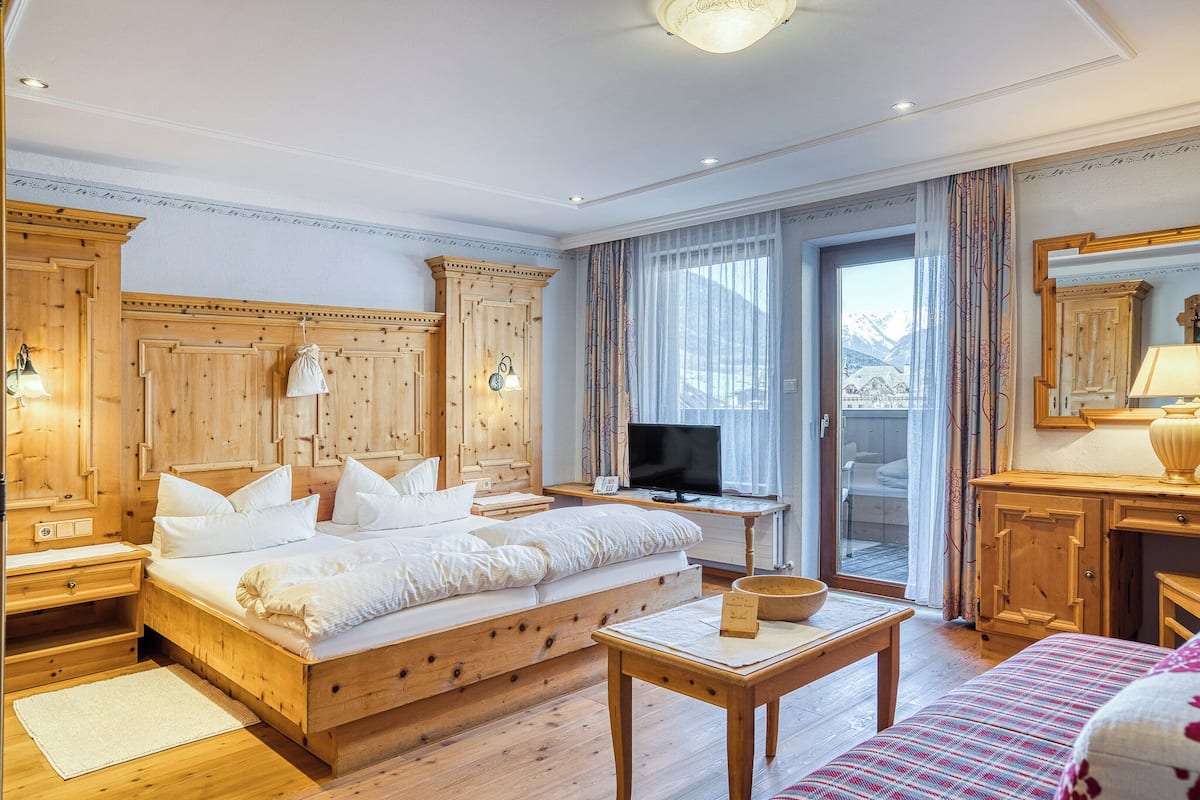 A wooden bedroom with a bed, a television, a desk, and a view of mountains through the window.
