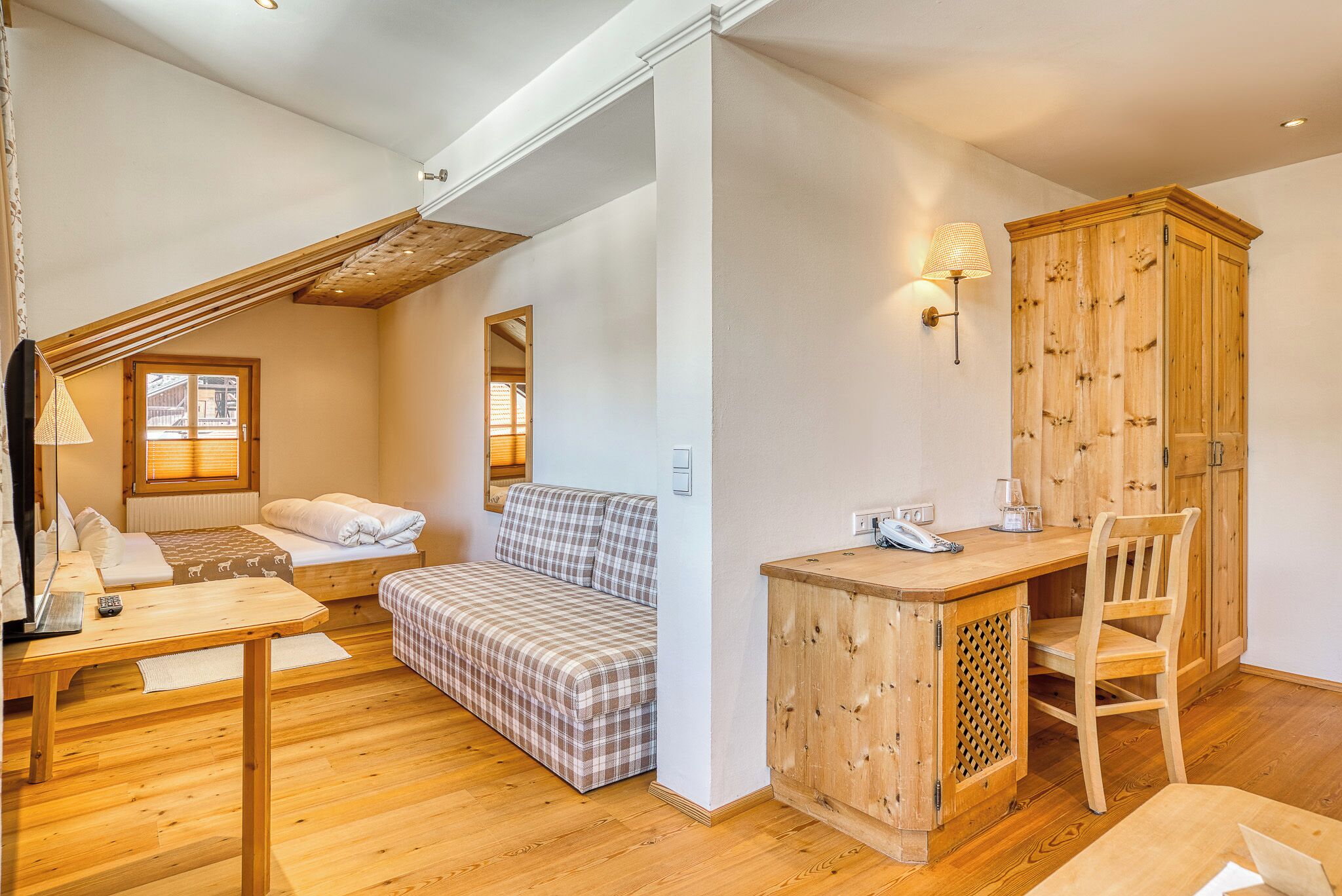 A cozy room with a bed, a sofa, a desk, and a wooden cabinet.