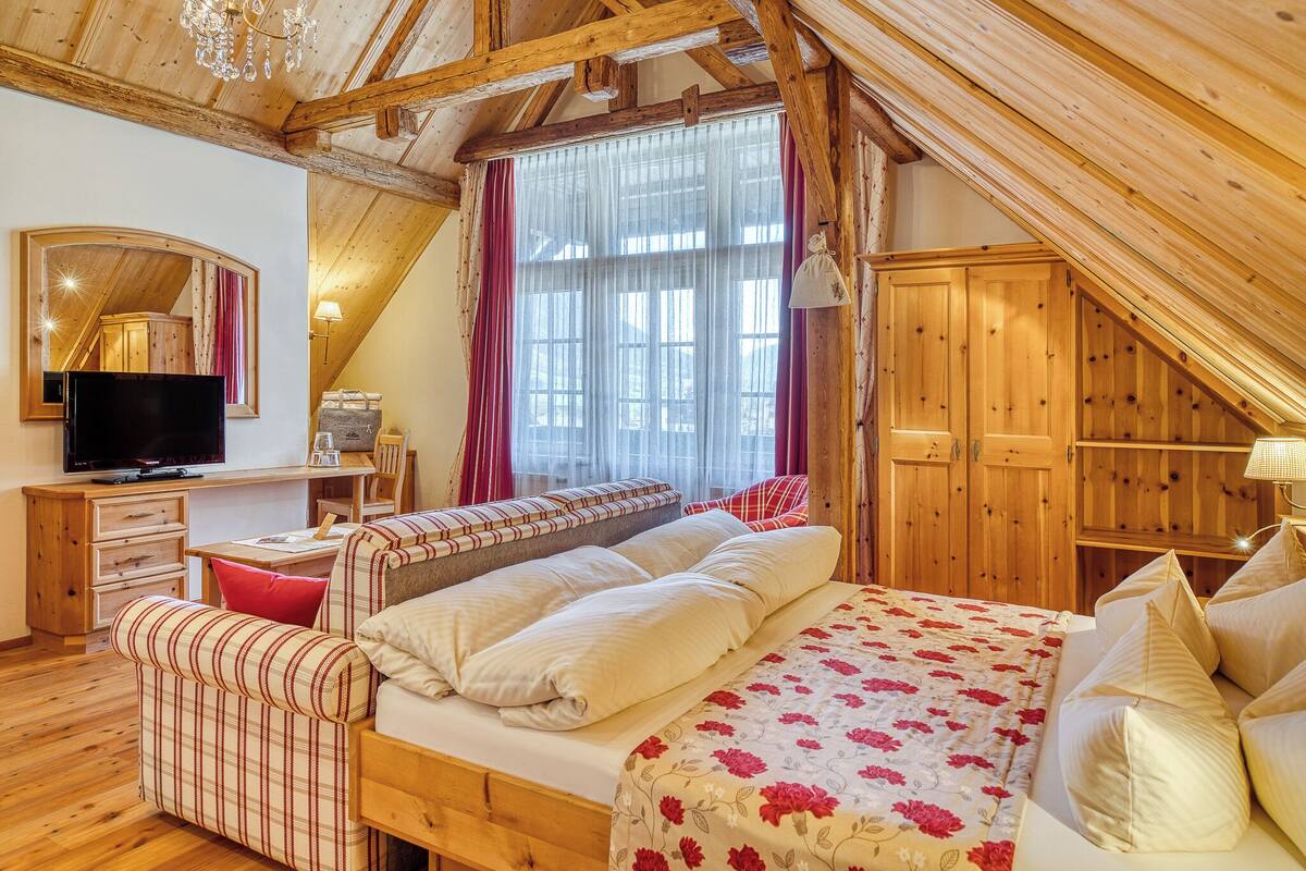 A cozy room with a bed, a TV, a desk, and a wooden ceiling.