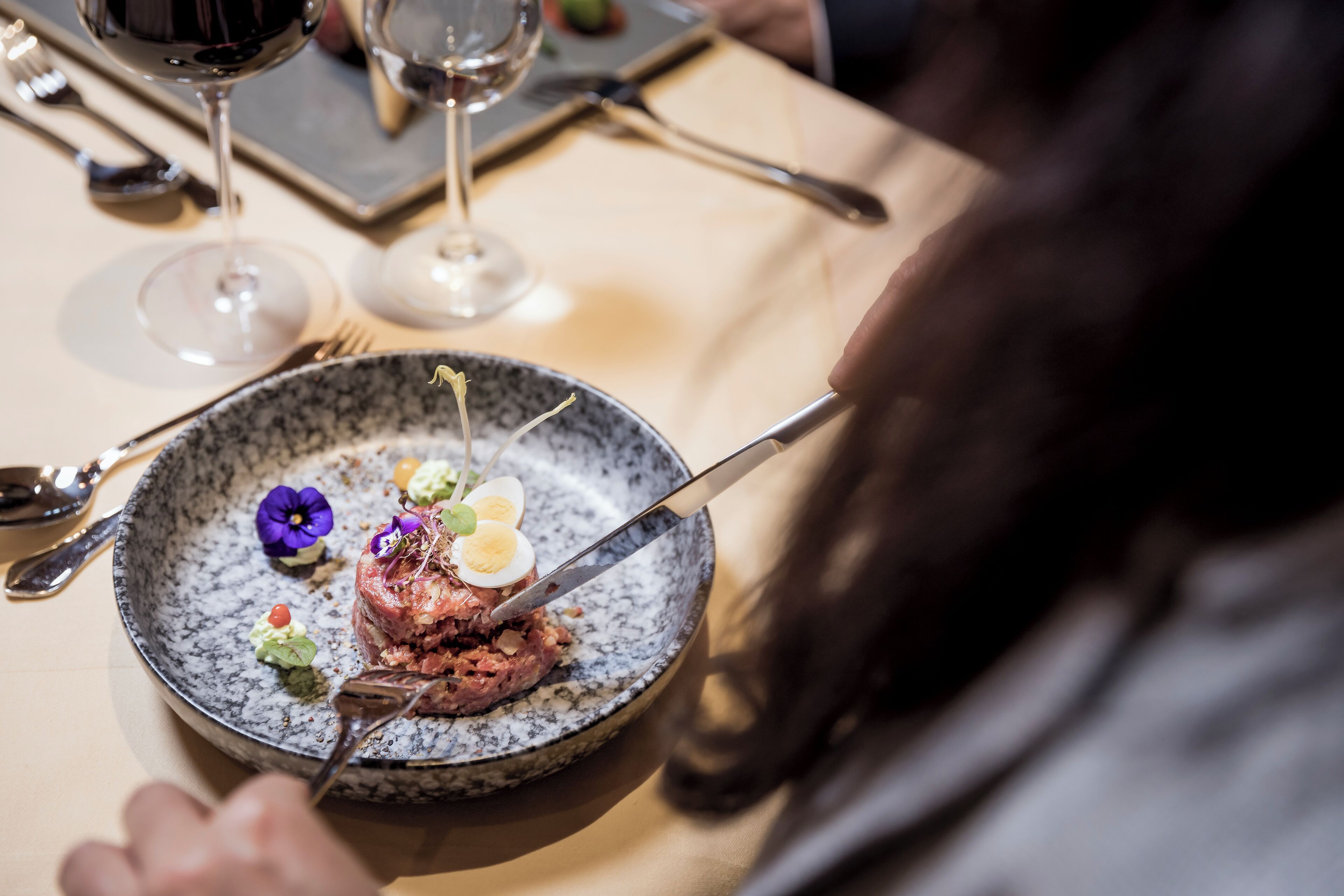 A dining table with a plate of food, a fork, and a wine glass.