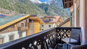 A balcony with wicker furniture, a wooden railing, and a view of mountain houses.