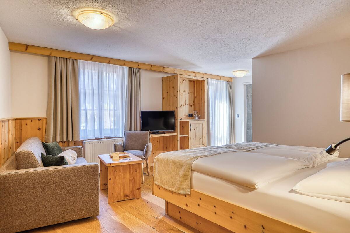 A hotel room with a bed, a sofa, a desk, a television, and wooden paneling.